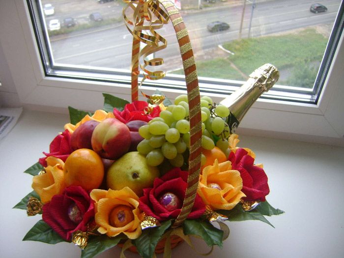 На дно сначала ставится шампанское, затем ряд фруктов. Конфеты, завернутые в кринкл-бумагу в форме лепестков цветка, укладываются по краю.